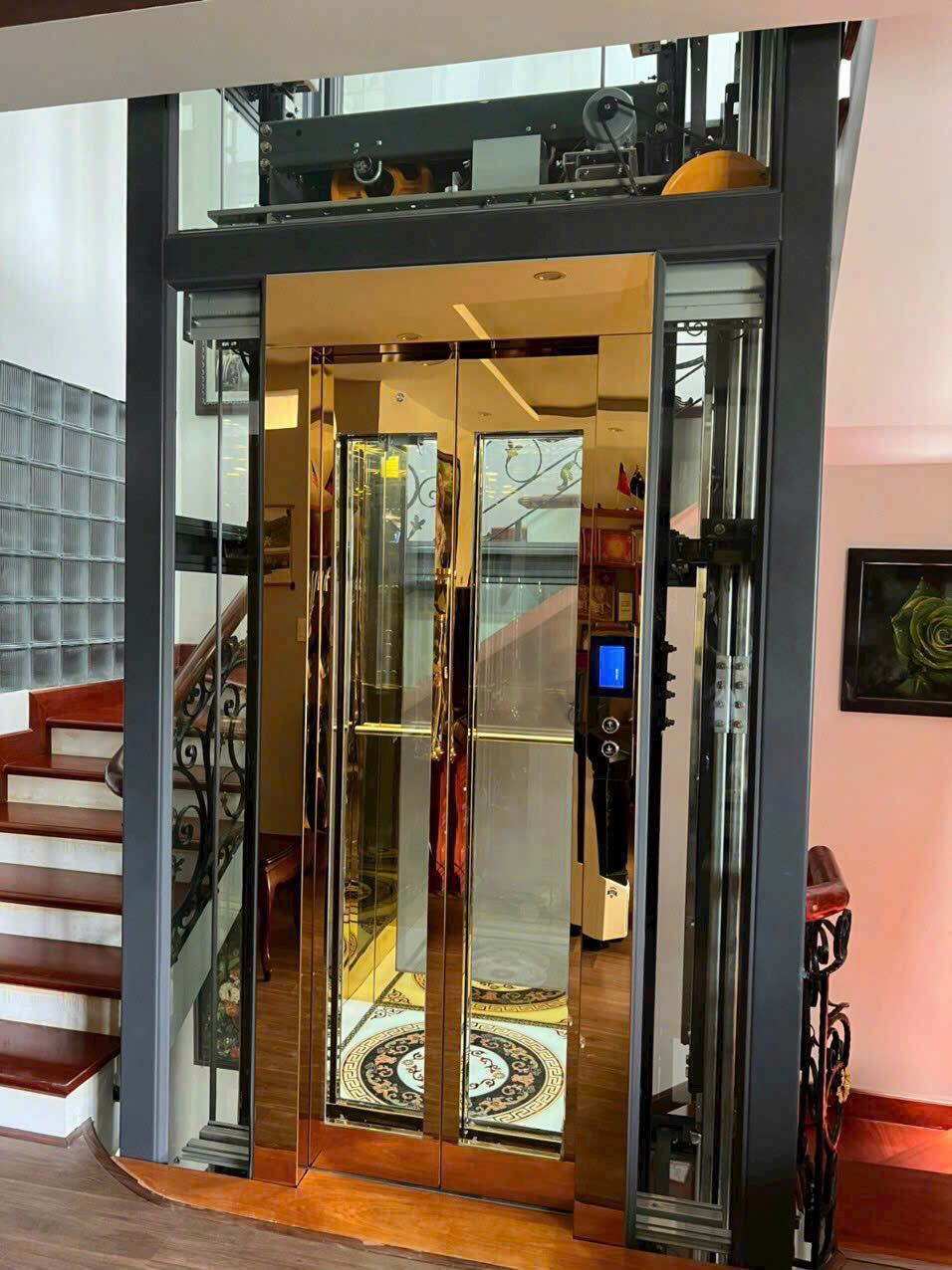 Thang máy gia đình vách kính khung thép, cửa inox mạ vàng sang trọng cạnh cầu thang gỗ
